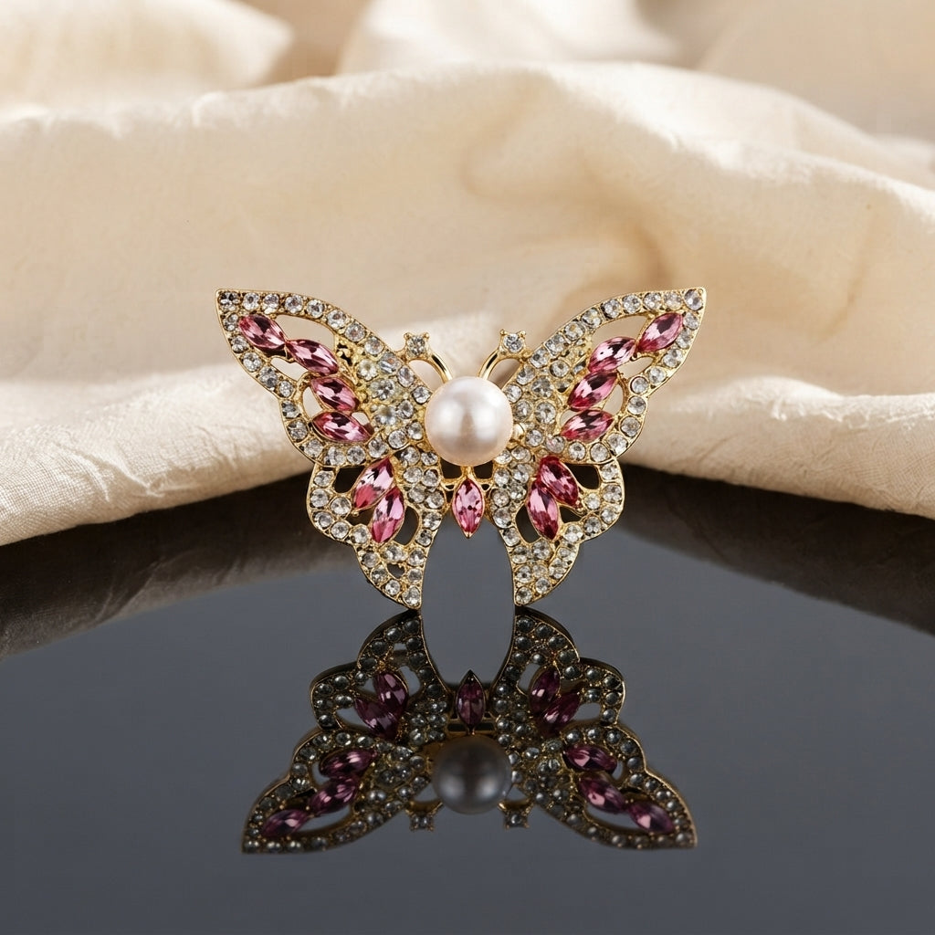 Gold Pearl Butterfly Crystal Brooch in Champagne Gold on dark grey mirror surface with cream silk backdrop showing large butterfly brooch with open filigree gold wings dense micro-pave white CZ border champagne marquise crystal wing stones and large faux pearl centre with mirror reflection below and warm bokeh lights in background