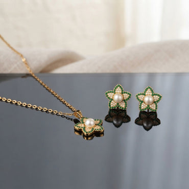 Gold Pearl and CZ Star Flower Pendant Necklace and Stud Earrings Set in Emerald Green on grey slate mirror with cream linen backdrop showing 18K gold cable chain with 5-petal star flower pendant with emerald green micro-pave CZ border champagne CZ inner petals freshwater pearl centre and matching star flower stud earrings