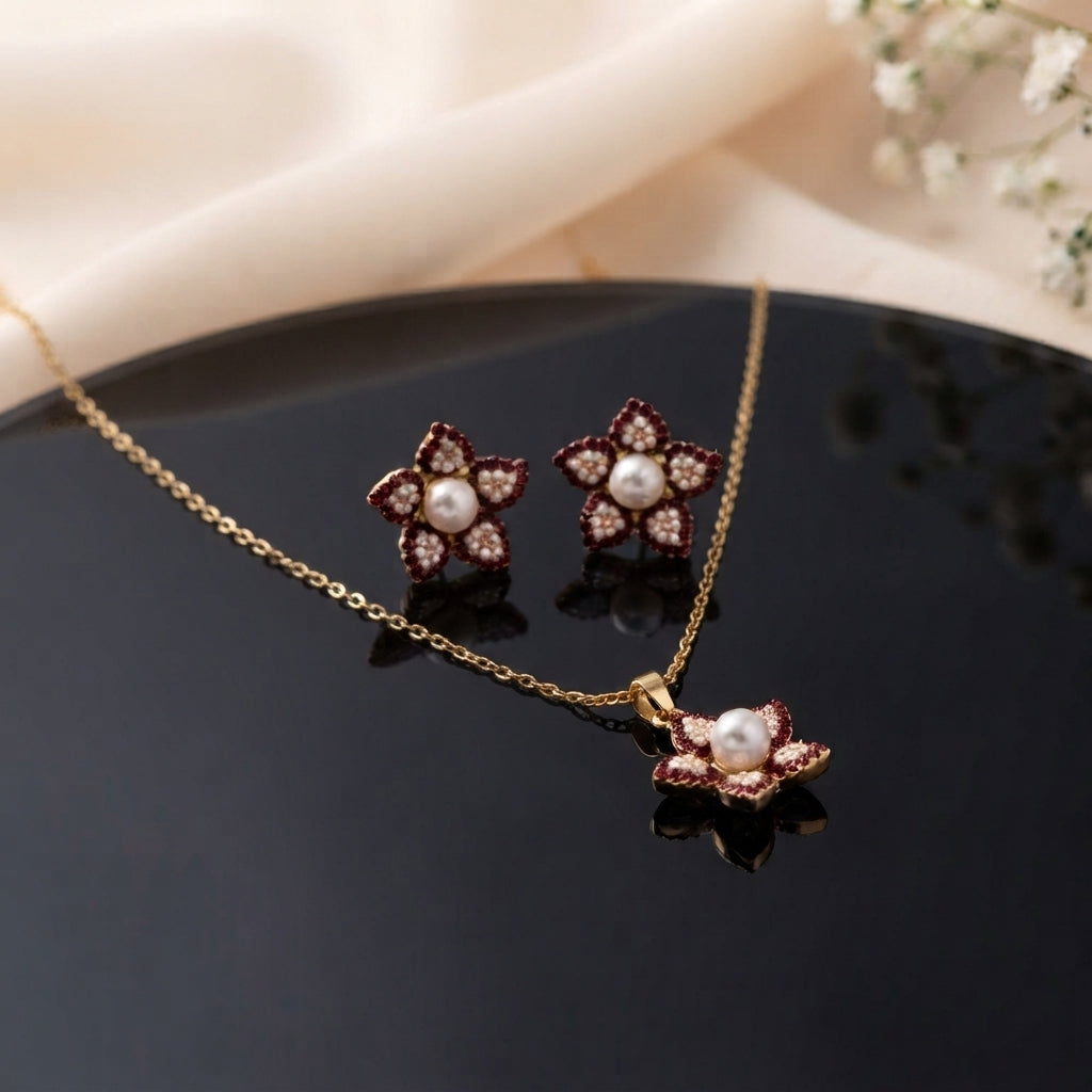Gold Pearl and CZ Star Flower Pendant Necklace and Stud Earrings Set in Ruby Burgundy on black ceramic plate with cream fabric and baby breath flowers showing 18K gold cable chain with 5-petal star flower pendant with deep ruby burgundy micro-pave CZ border champagne CZ inner petals freshwater pearl centre and matching star flower stud earrings