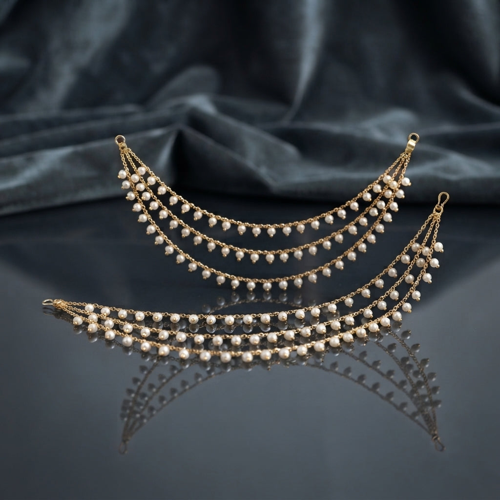 Gold Pearl Drop Multi-Strand Sahara Earrings Pair product shot on dark grey mirror surface with blue silk fabric backdrop showing two 4-strand cascading crescent swag gold cable chain earrings with evenly spaced round faux pearl drops and hook loop attachment ends with mirror reflections below