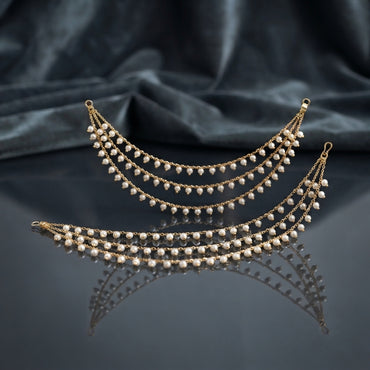 Gold Pearl Drop Multi-Strand Sahara Earrings Pair product shot on dark grey mirror surface with blue silk fabric backdrop showing two 4-strand cascading crescent swag gold cable chain earrings with evenly spaced round faux pearl drops and hook loop attachment ends with mirror reflections below