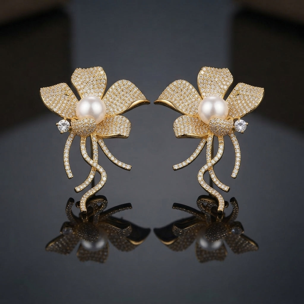 Gold Pearl Pave Orchid Flower Vine Statement Earrings pair on dark grey mirror surface showing large 5-petal orchid magnolia flower fully encrusted in dense micro-pave champagne yellow CZ stones with large round faux pearl cabochon centre white CZ side accent and curling vine tendril stems with full micro-pave CZ draping below in 18K gold-tone plating with mirror reflections below