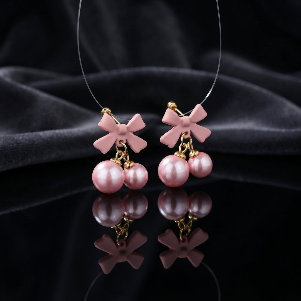 Gold Pink Bow Double Pearl Drop Earrings pair — matte blush pink resin bow studs with double blush rose pink simulated pearl cherry drops on gold links, luxury flat-lay on dark charcoal silk backdrop with mirror reflection