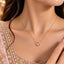 Gold Pink CZ Heart Bezel Solitaire Pendant Necklace close-up worn by bridal model in blush pearl-embroidered lehenga with gold bokeh backdrop