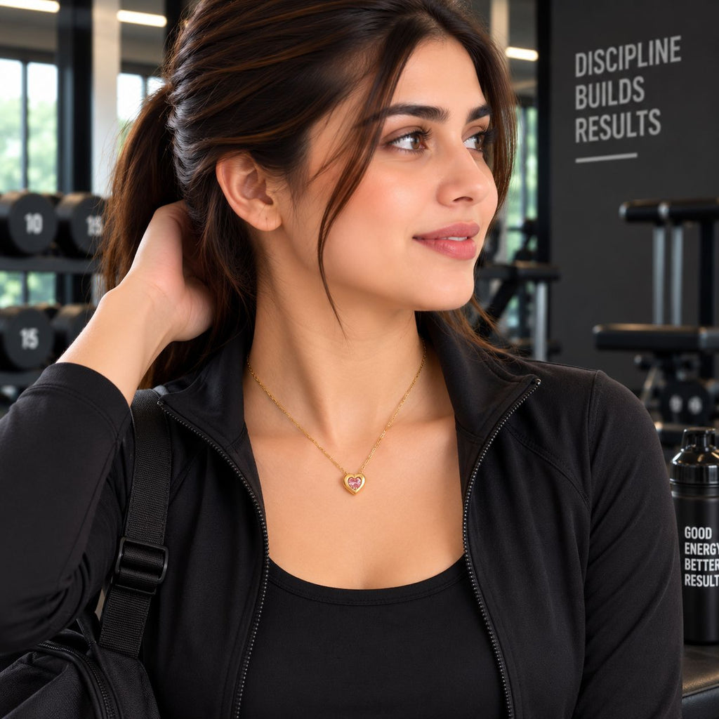 Gold Pink CZ Heart Bezel Solitaire Pendant Necklace worn by model in black gym jacket at gym setting with dumbbell rack backdrop