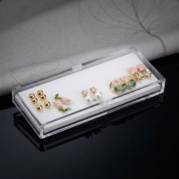 Gold Pink Floral Enamel Pearl CZ 4-Pair Stud Earring Set flat lay on black mirror surface showing gold double ball studs pink tulip enamel studs with green leaf CZ pearl drop studs and large gold hoop with pink floral enamel scene and pink flower cluster CZ top with mirror reflections below