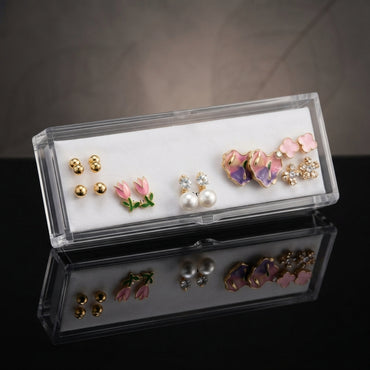 Gold Pink Purple Floral Enamel Pearl CZ 4-Pair Stud Earring Set flat lay on black velvet tray with grey fabric backdrop showing gold double ball studs pink tulip enamel studs white CZ pearl drop studs and large purple iridescent floral enamel petal stud with pink clover and CZ snowflake cluster with mirror reflections below