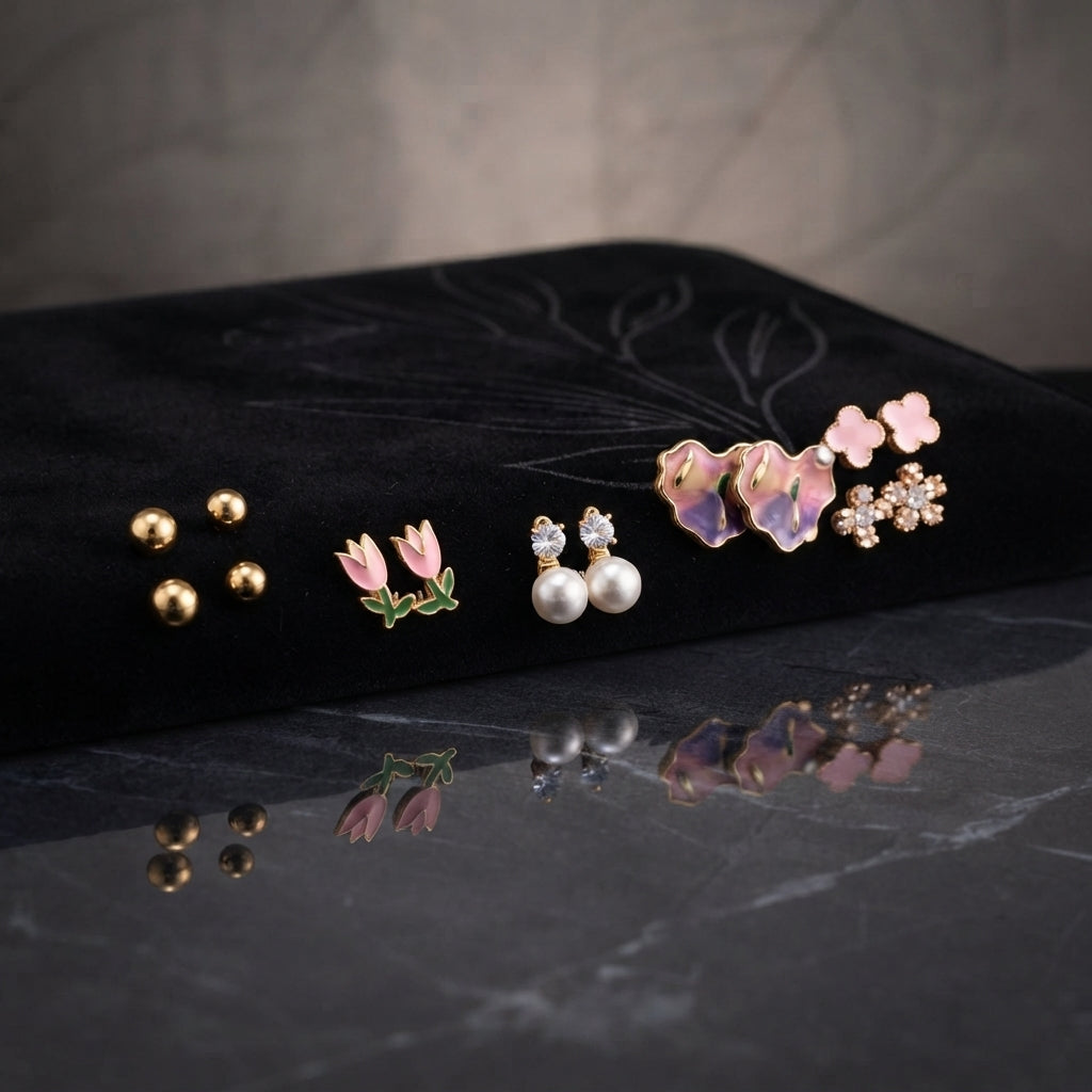 Gold Pink Purple Floral Enamel Pearl CZ 4-Pair Stud Earring Set displayed in open clear acrylic gift box on black mirror surface with grey fabric backdrop showing all four pairs arranged on white velvet insert with mirror reflection below
