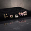 Gold Pink Purple Floral Enamel Pearl CZ 4-Pair Stud Earring Set displayed in open clear acrylic gift box on black mirror surface with grey fabric backdrop showing all four pairs arranged on white velvet insert with mirror reflection below