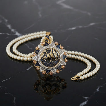 gold-plated double strand pearl necklace with a circular pendant featuring Arabic Allah calligraphy surrounded by a sunburst crystal halo, shown on a dark reflective surface.