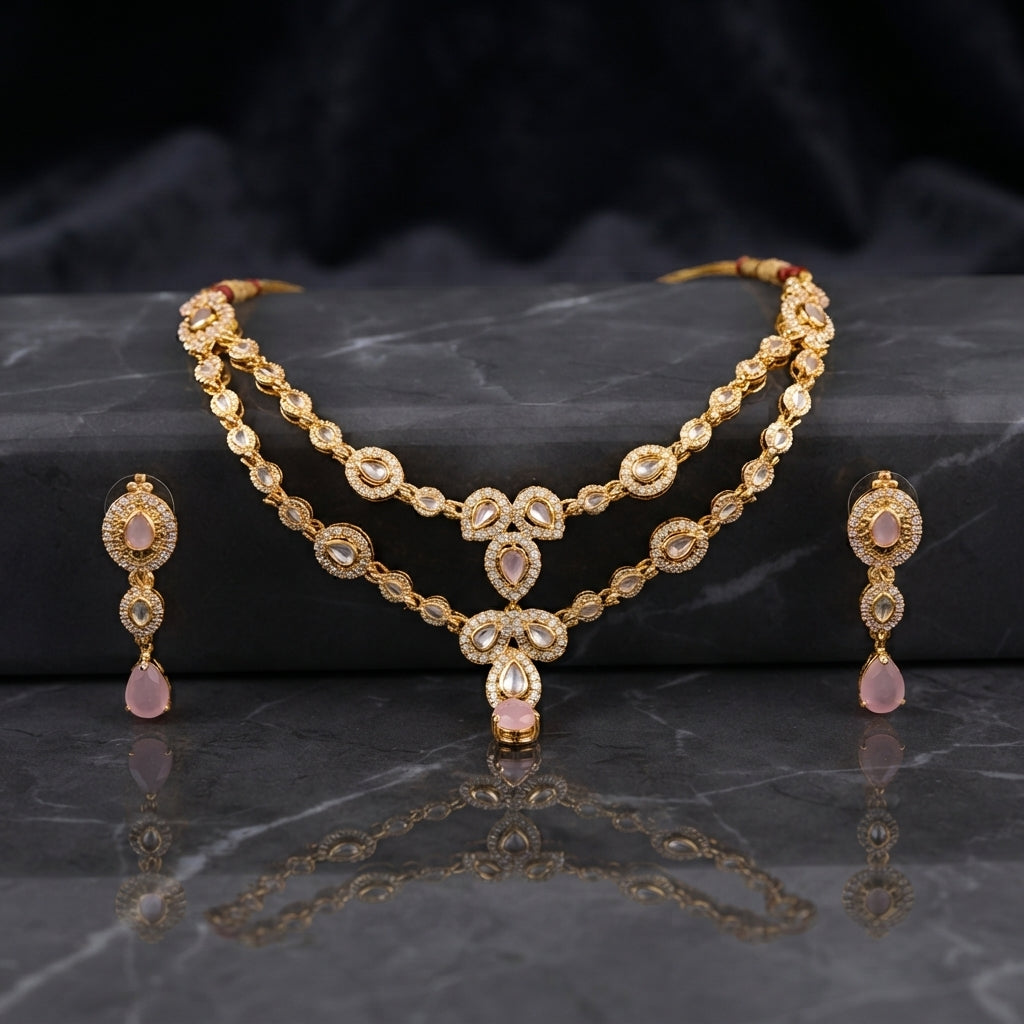 Gold Polki and Rose Quartz Double Layer Necklace and Drop Earrings Bridal Set — 22K antique gold-tone 2-piece Mughal bridal set with double-layer rigid polki simulant teardrop necklace with white CZ micro-pavé halos and rose quartz pear pendant drop and matching 3-tier polki and rose quartz drop earrings displayed on dark grey marble surface with black satin backdrop