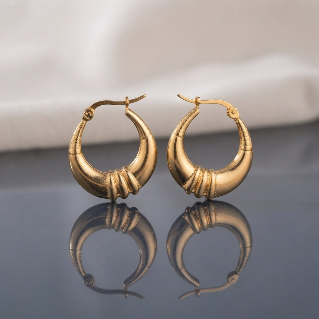 Gold PVD Stainless Steel Crescent Basket Hoop Earrings with Ribbed Knot Accent pair standing side by side on dark grey mirror surface with soft warm cream ivory fabric backdrop showing 18K gold PVD coated stainless steel wide crescent basket hoops with graduated puffy crescent body and decorative ribbed rope-cut knot wrap accent at widest point mirror-polish finish with French lever closure and sharp mirror reflection below