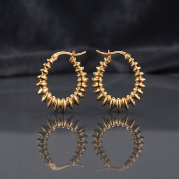 Gold PVD Stainless Steel Layered Disc Rondelle Spike Hoop Earrings pair on dark mirror surface with charcoal slate satin backdrop showing 18K gold PVD coated stainless steel statement hoops with continuous layered flat disc rondelle beads fanned in spike sunburst clusters tightly packed around full hoop circumference with sharp mirror reflection below