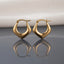 Gold PVD Stainless Steel Puffy Angular Shield V-Point Geometric Hoop Earrings pair standing side by side on light grey mirror surface with soft warm cream ivory fabric backdrop showing 18K gold PVD coated stainless steel hoops with chunky puffy inflated body in wide-bottom shield arrowhead V-point silhouette mirror-polish finish with French lever closure and sharp mirror reflection below