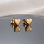 Gold PVD Stainless Steel Smooth Puffy Heart Stud Earrings pair side by side on dark grey ceramic mirror surface with soft warm cream ivory fabric backdrop showing 18K gold PVD coated stainless steel dainty studs with smooth 3D puffy inflated mirror-polish heart face and butterfly push-back post with sharp mirror reflection below