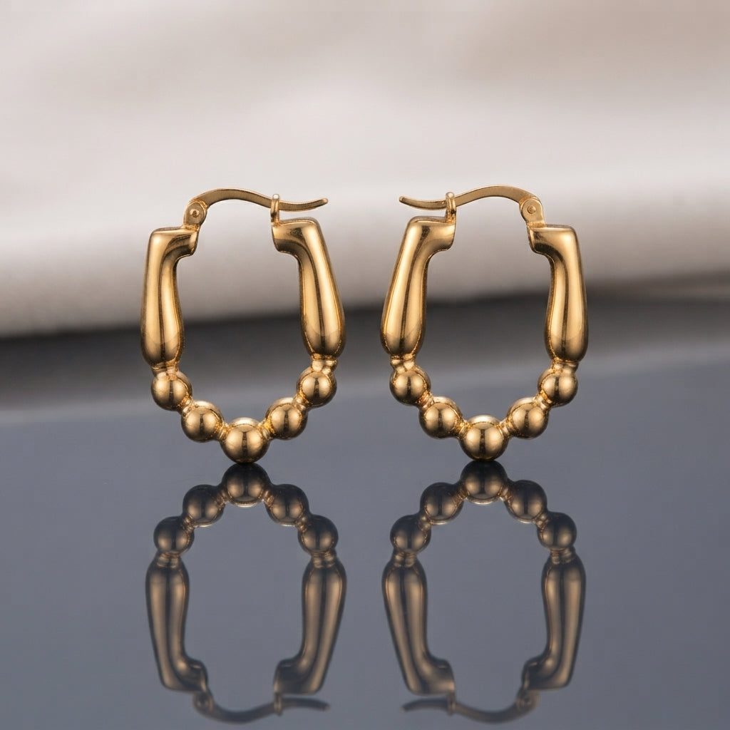Gold PVD Stainless Steel Split Hoop Earrings with Smooth Tube Top and Ball Bead Chain Bottom pair standing side by side on dark grey mirror surface with soft warm cream ivory fabric backdrop showing 18K gold PVD coated stainless steel hoops with chunky smooth flat-top rectangular tube upper frame and 6 to 7 smooth round gold ball beads scalloped lower arc mirror-polish finish with French lever closure and sharp mirror reflection below