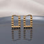 Gold PVD Stainless Steel Square Ball Bead Hoop Earrings pair standing side by side on dark grey ceramic mirror surface with soft warm cream ivory fabric backdrop showing 18K gold PVD coated stainless steel perfect square hoops made of 9 to 10 smooth round mirror-polish gold ball beads with French lever latch-back closure and sharp mirror reflection below