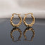 Gold PVD Stainless Steel Twisted Rope Hoop Earrings with Heart Accent pair standing side by side on dark grey mirror surface with soft warm cream ivory fabric backdrop showing 18K gold PVD coated stainless steel hoops with two thick satin-brushed twisted rope braided strands and smooth puffy mirror-polish 3D heart accent at base with French lever closure and sharp mirror reflection below