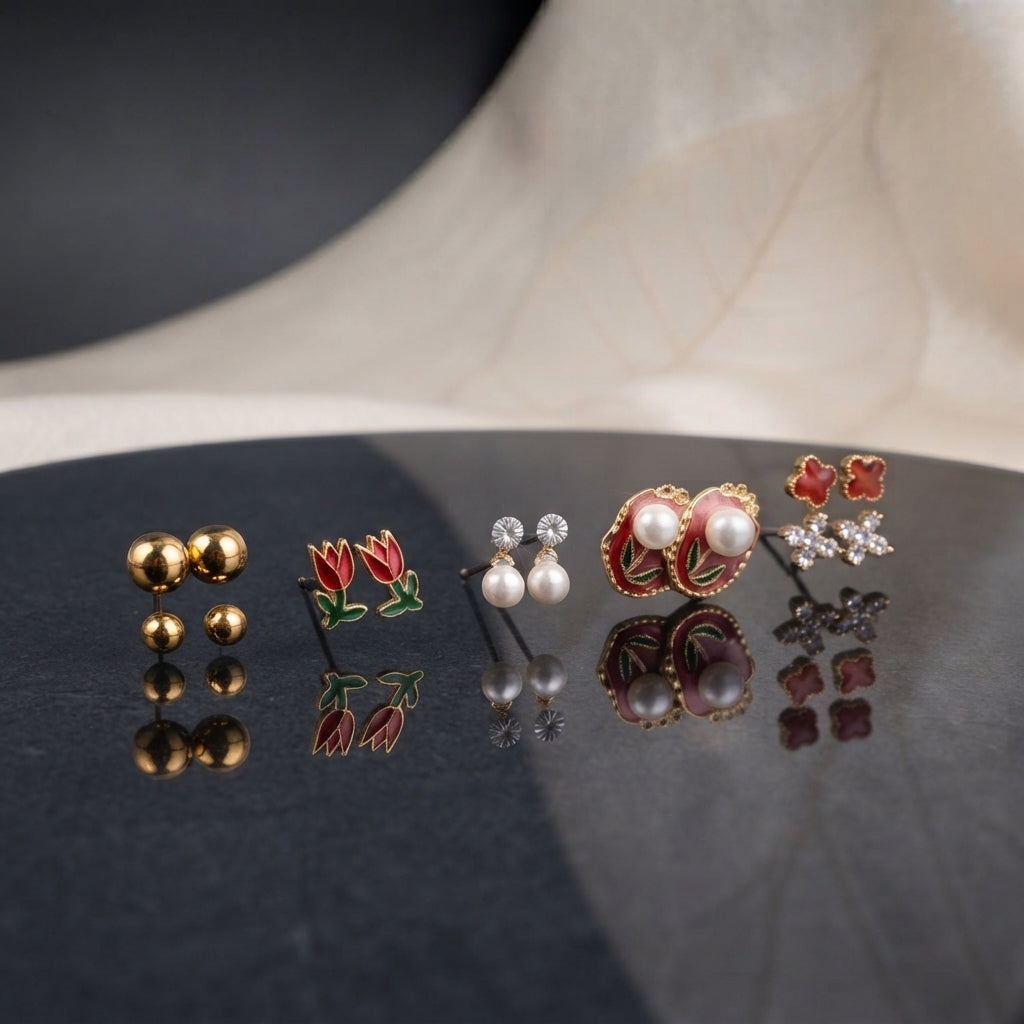 Gold Red Tulip Floral Enamel Pearl CZ 4-Pair Stud Earring Set displayed in clear acrylic gift box on black marble surface with beige backdrop showing gold ball studs red tulip enamel studs silver CZ pearl drop studs and large red burgundy enamel oval stud with faux pearls red clover and CZ snowflake cluster with mirror reflection below