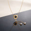 Gold Roman Numeral Circle Enamel Lariat Necklace in black enamel flat lay on grey and white split surface with gold cable chain showing circular Roman numeral engraved pendant with black enamel center and double drop lariat chain with cushion CZ bezel drops and mirror reflection below
