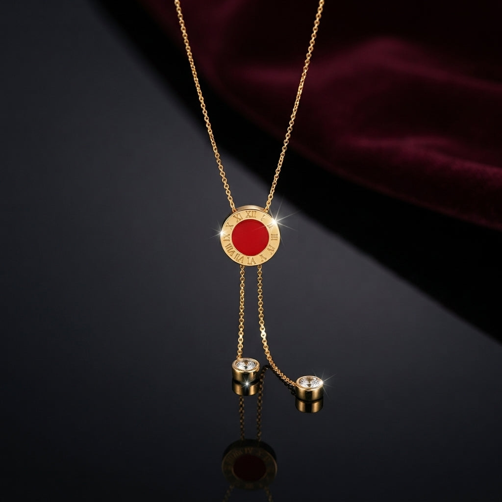Gold Roman Numeral Circle Enamel Lariat Necklace in red enamel flat lay on dark grey mirror surface with burgundy velvet backdrop showing circular Roman numeral engraved pendant with red enamel center and double drop lariat chain with round CZ bezel cylinder drops and mirror reflection below