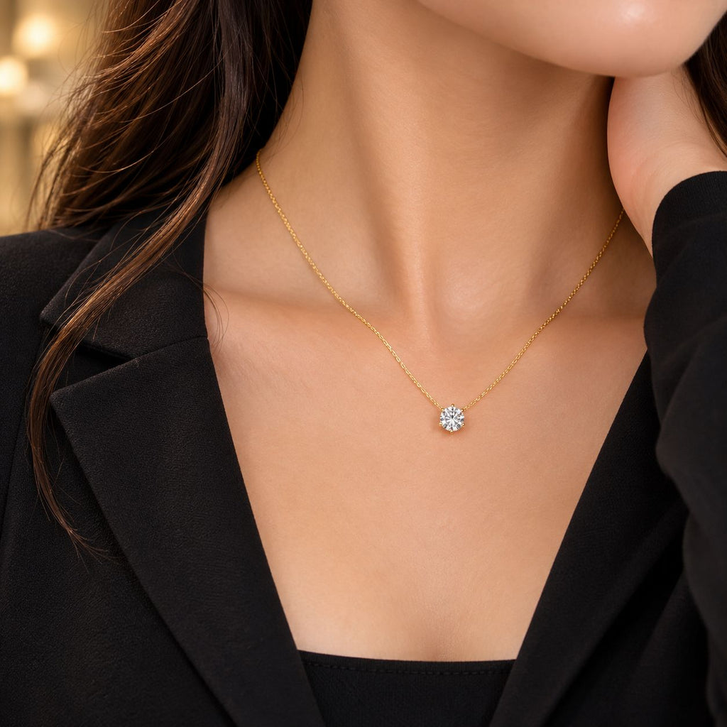 Gold Round Brilliant CZ Solitaire Floating Pendant Necklace close-up worn by model in black blazer with gold bokeh backdrop