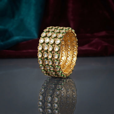 Gold Round Kundan Polki Green Enamel Wide Cuff Bangle Set of 4 standing upright on dark grey mirror surface with teal and burgundy velvet backdrop showing four matching wide gold bangles stacked as wide cuff with rows of round flat-cut CZ kundan polki stones in green enamel borders and gold filigree lattice interior with mirror reflection below