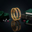 22K Gold-Tone Ruby Red CZ Cushion Bezel & Emerald Green Pavé Border Honeycomb Filigree Openwork & Triple-Row White CZ Wide Bangle Set of 2 on black mirror surface with loose ruby and emerald CZ stones, green velvet ribbon and dark marble book prop backdrop