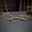 Gold Smooth Ball Bead Tassel Necklace Bracelet Earrings Set 3 Piece in 22K gold-tone plating on dark grey blue mirror surface with dark interior and gold glass jewellery box backdrop showing flat oval link chain necklace with large smooth gold ball drop pendant double-wire expandable bangle with smooth graduated gold ball beads and large smooth round gold dome ball stud earrings with mirror reflections below