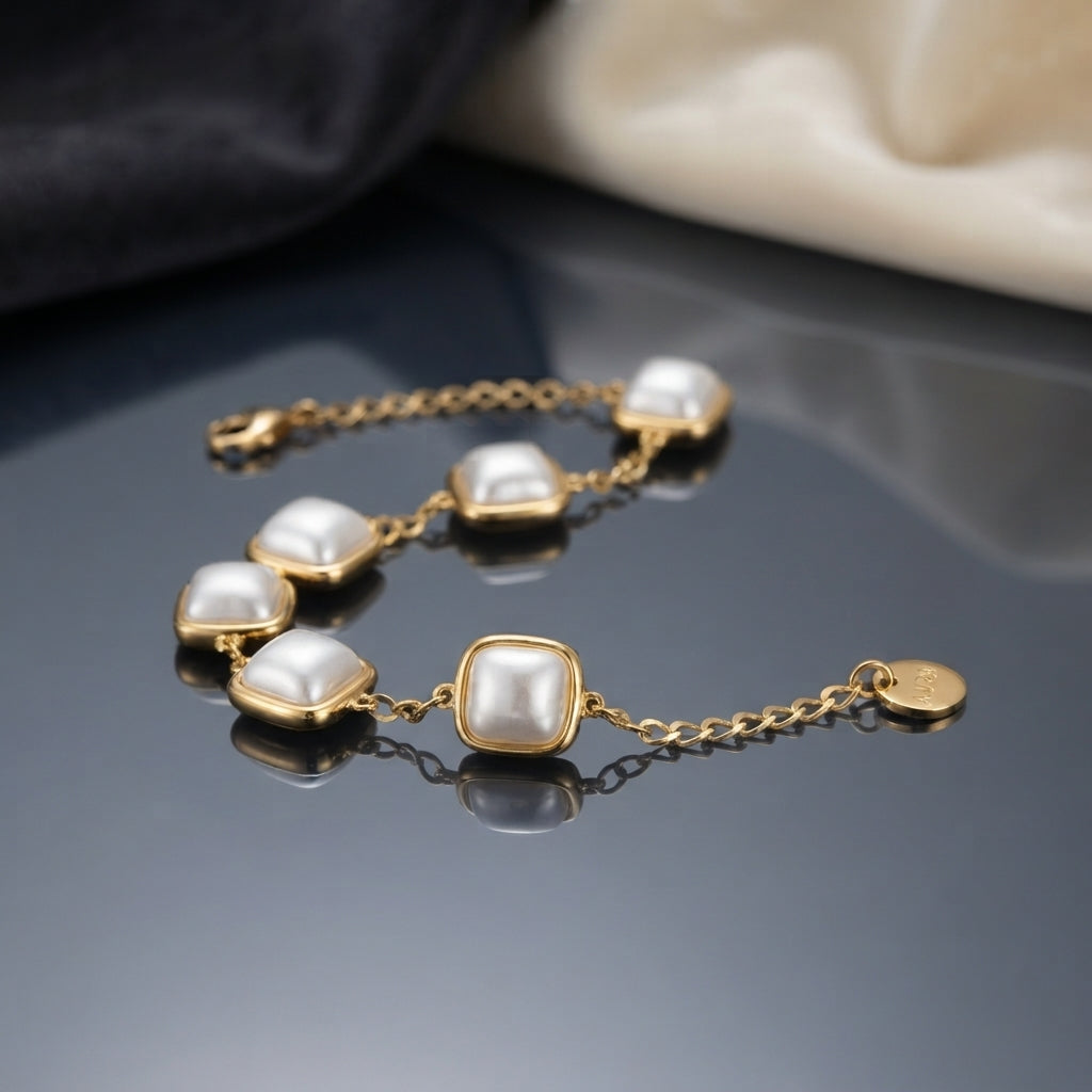 Gold Square Cushion Faux Pearl Bezel Station Bracelet detail shot on grey mirror surface with dark and cream silk backdrop showing six square cushion faux pearl stations in gold-tone bezel settings on gold rolo chain with extension chain and mirror reflection below