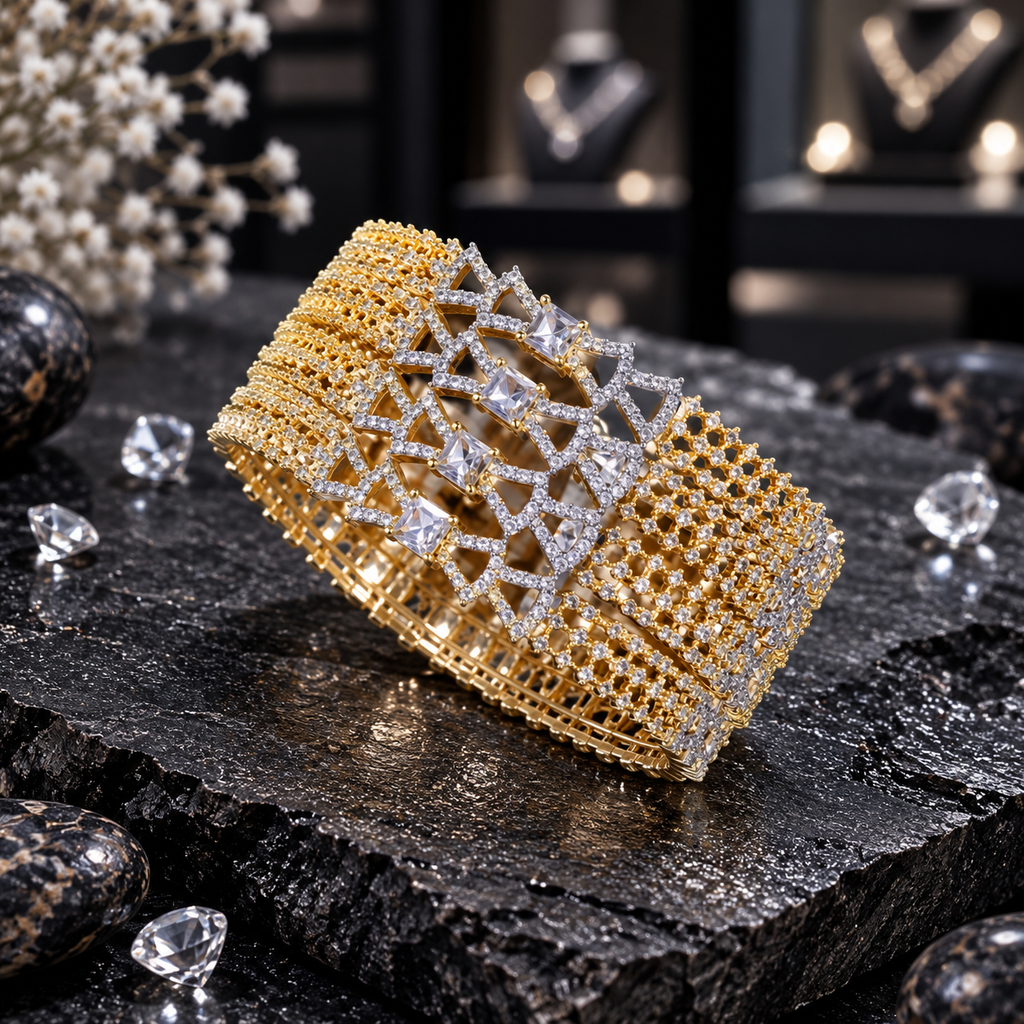 Four matching gold-tone AD bangles with square clear centre accents, angular clear-accent frames and lattice-style side sections on dark stone.