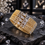 Four matching gold-tone AD bangles with square clear centre accents, angular clear-accent frames and lattice-style side sections on dark stone.