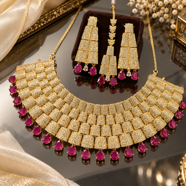 Gold-tone American diamond bridal necklace with rectangular panels and deep pink teardrop accents, matching long earrings and maang tikka.