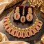 Gold-tone American diamond necklace with deep red center stones and clear oval halos, matching long earrings and leaf-detailed maang tikka.