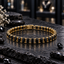 Gold-tone linked bracelet with faceted black rectangular accents, visible prong details and a rectangular back closure section, arranged in an oval on dark slate.