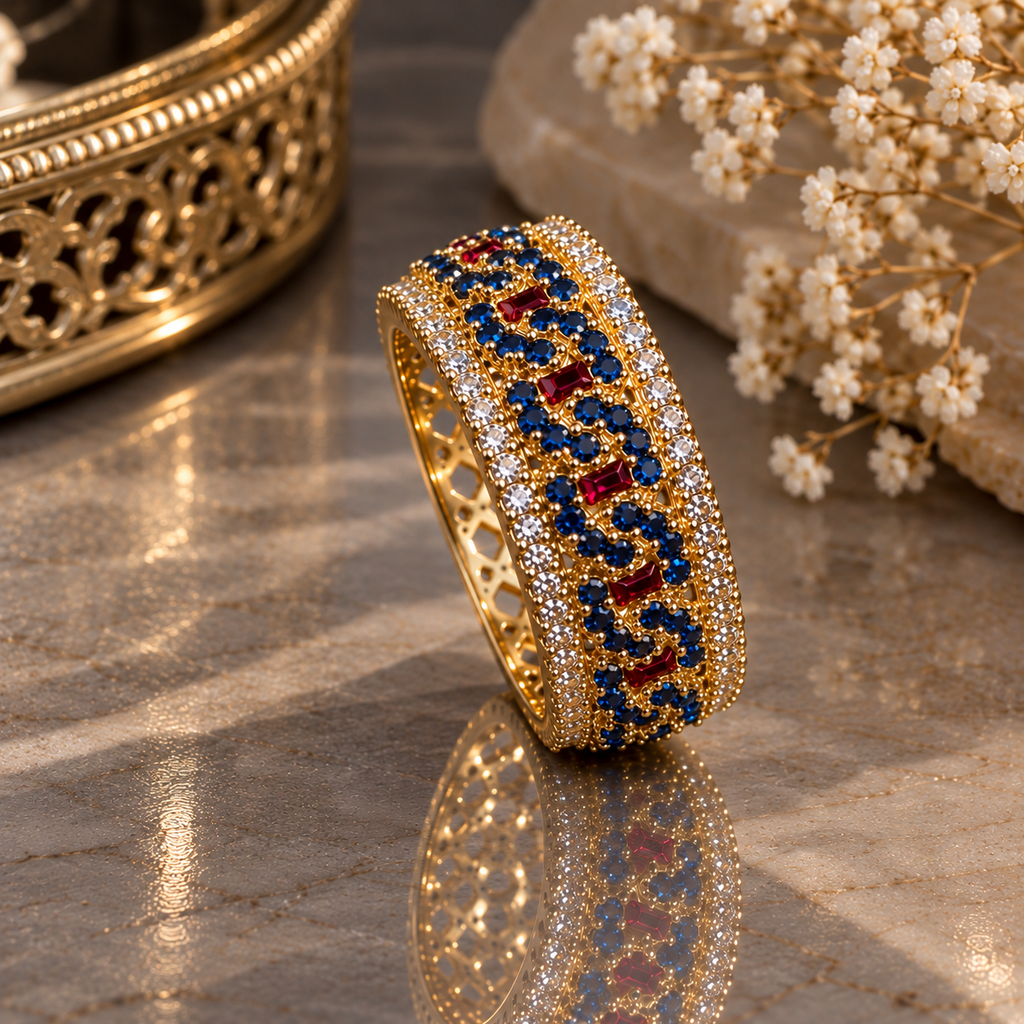 Gold-tone ornate band ring with small dark-blue round accents, red rectangular accents, clear-accent borders and openwork sides.