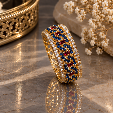 Gold-tone ornate band ring with small dark-blue round accents, red rectangular accents, clear-accent borders and openwork sides.