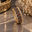 Gold-tone ornate band ring with small dark-blue round accents, red rectangular accents, clear-accent borders and openwork sides.