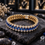 Gold-tone linked bracelet with diagonal blue rectangular accents, round clear accents along both borders and a rectangular back closure section on dark slate.