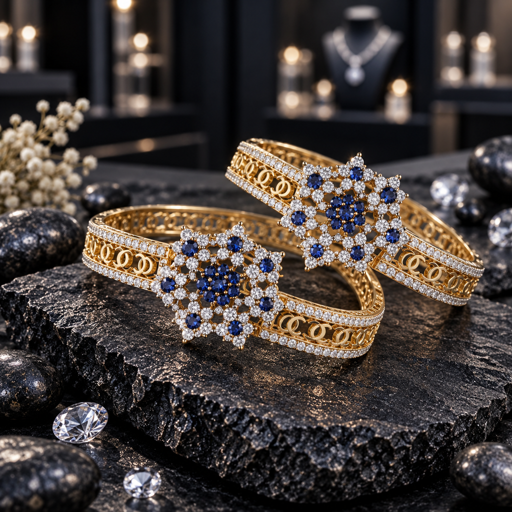 Pair of gold-tone openwork bangles with dark blue floral clusters and clear accent borders, displayed on dark slate.