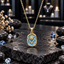 Gold-tone tulip pendant necklace with a textured blue background, raised flower and leaf motif, and rounded rectangular border.