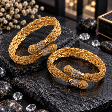 Pair of gold-tone open-ended cuff bracelets with braided mesh-style bands, clear accented cylindrical ends and rounded bead-textured caps.