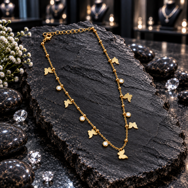 Gold-tone fine chain necklace with flat butterfly charms, round clear accents in circular settings, small bead details, a lobster-style clasp and extension chain, displayed on dark slate.