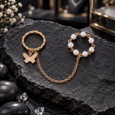 Gold-tone twisted-rope-look butterfly ring connected by an oval-link chain to a white pearl-look bead ring, displayed flat.