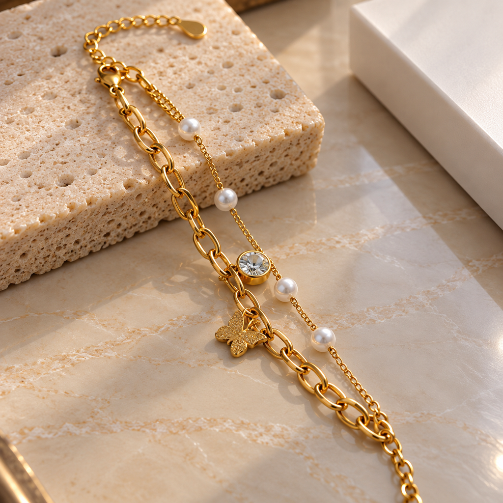 Gold-tone double-chain bracelet with elongated oval links, four ivory-white pearl-look beads, a textured butterfly charm and a round clear accent.