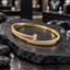 Gold-tone oval bangle with overlapping clear round accent rows, textured borders and an upright rectangular clear-accent centre detail, displayed on dark slate.
