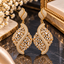Gold-tone openwork drop earrings with leaf-like tops, tapered rectangular clear accents and sweeping S-shaped clear-accent bands.