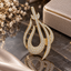 Gold-tone curved teardrop pendant with clear accents, sweeping asymmetric outlines, openwork crossbars and an elongated hanging loop.