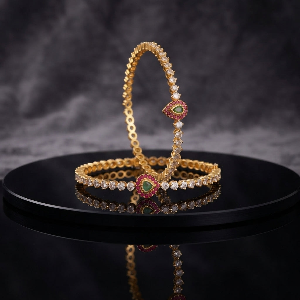Gold-Tone CZ Tennis Slim Bangle Pair with Multi-Color Teardrop CZ Focal Clasp displayed upright and flat on black lacquer round stand with dark grey marble backdrop showing two matching slim gold bangles with continuous single row round white CZ prong-set stones and heart teardrop focal clasp with emerald-green CZ center ruby-red CZ halo and white CZ outer border with mirror reflection below