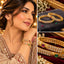 Gold-Tone Double-Row CZ Pave Multi-Color Oval CZ Accent Wide Bangle Pair worn on model wrist in beige embroidered bridal outfit with collage showing close-up on charcoal velvet tray with white gypsophila flowers and macro detail of double row white CZ pave with oval ruby-red and emerald-green CZ accents on gold sunburst divider bangles on burgundy velvet